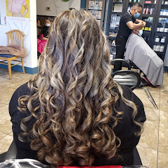 A woman with curly hair in a salon, another getting a haircut in the background