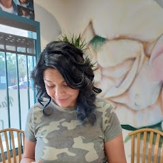 A woman in a camo shirt, mural and chairs in the background.